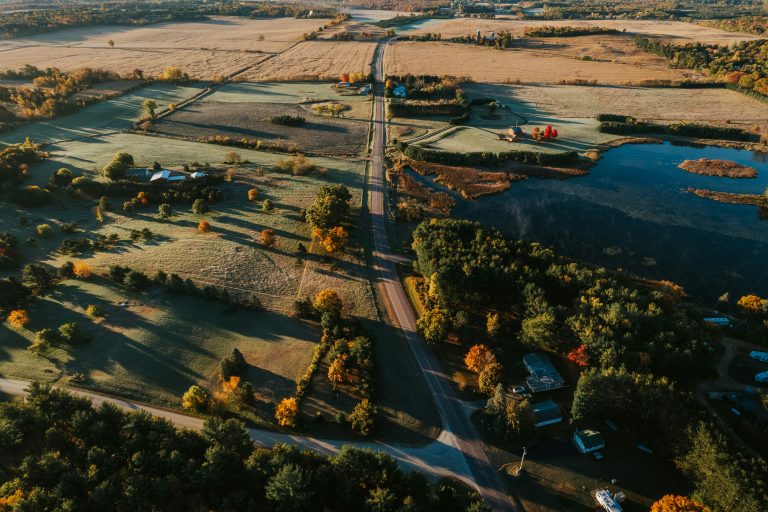 An aerial view of rural Wisconsin — a country road threading between farm fields and woodland, with a river winding through.