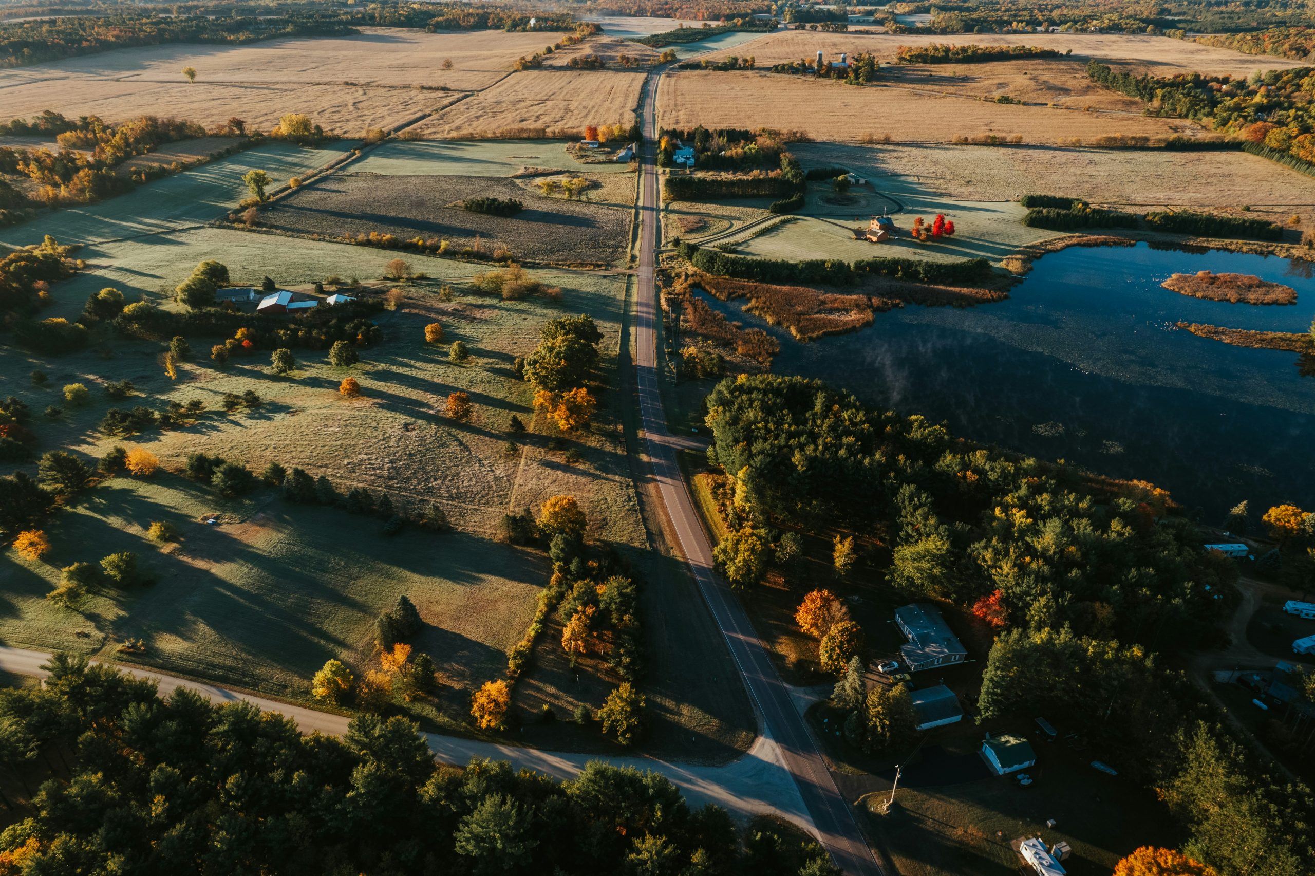 An aerial view of rural Wisconsin — a country road threading between farm fields and woodland, with a river winding through.