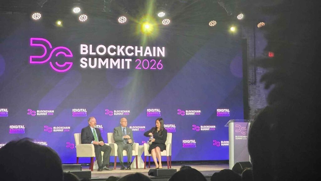 A panel on stage at the DC Blockchain Summit 2026, beneath a large screen reading Blockchain Summit 2026 with The Digital Chamber's logo.