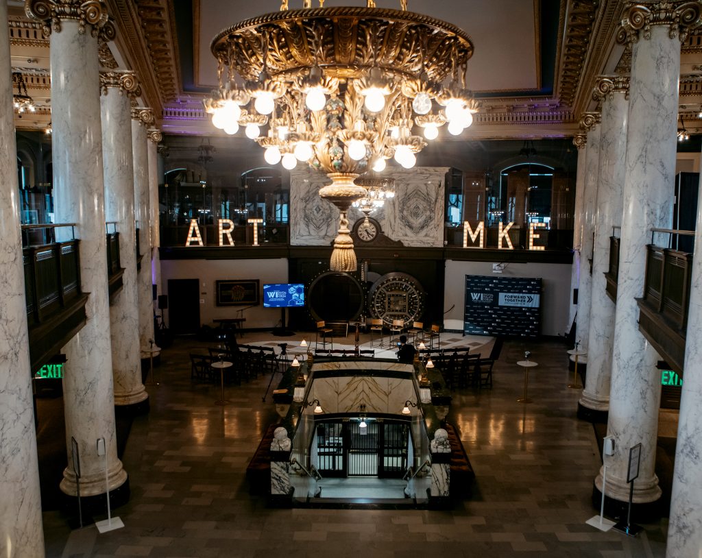 The main hall of the Milwaukee County Historical Society set for the forum, chandeliers lit and illuminated ART MKE letters above the balcony.