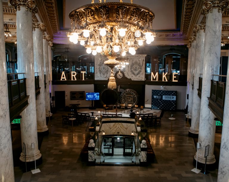 The main hall of the Milwaukee County Historical Society set for the forum, chandeliers lit and illuminated ART MKE letters above the balcony.