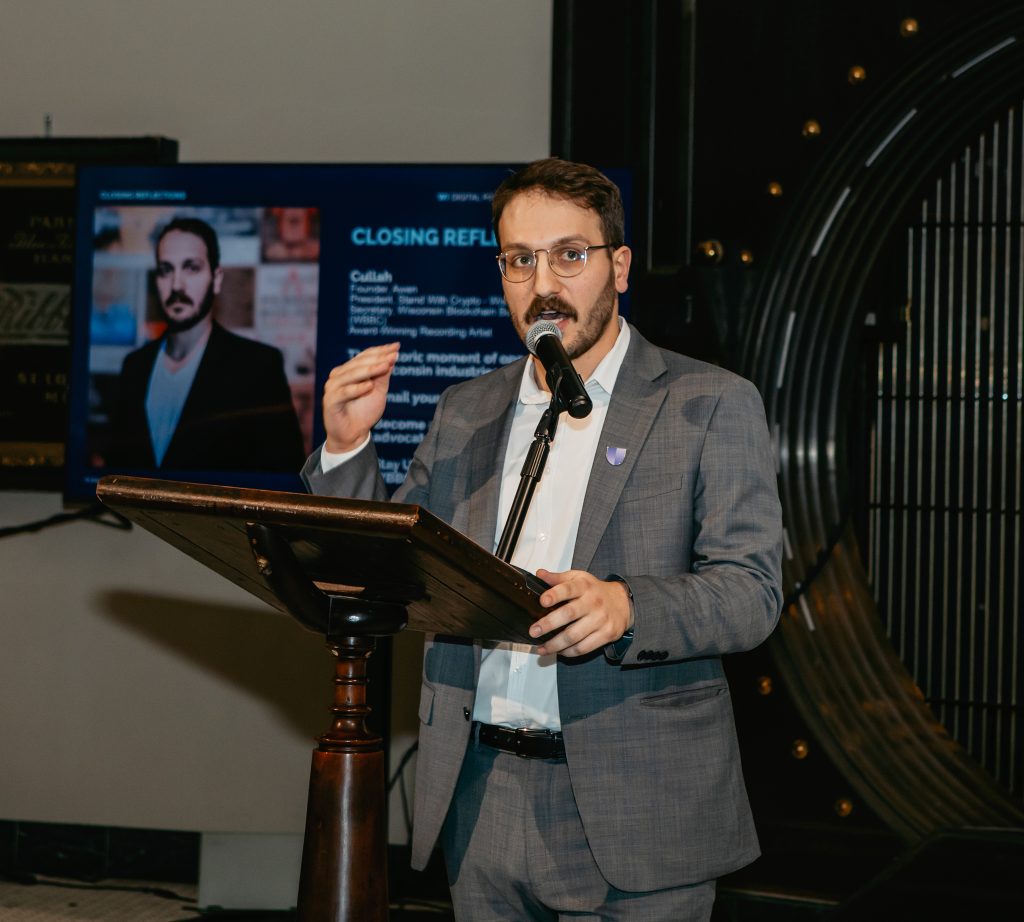 A speaker at the podium delivering closing reflections, presentation slide on the screen behind.