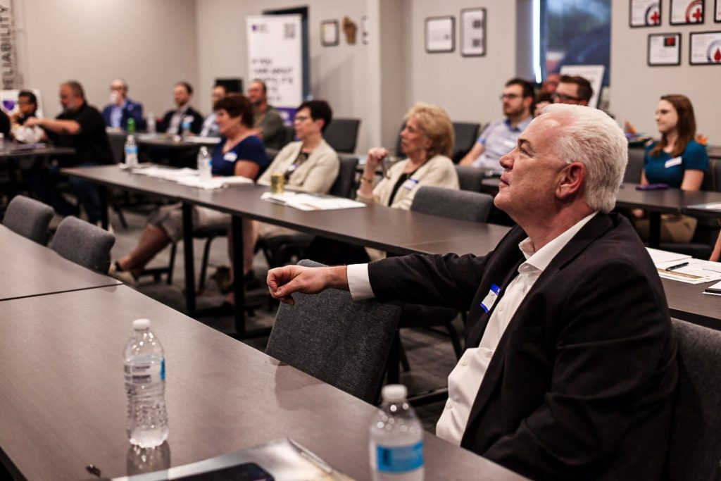 Attendees seated around long tables in the meeting room, turned toward the front.