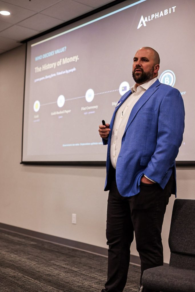 A speaker presenting in front of a slide titled The History of Money.